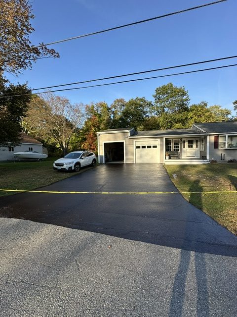 Freshly seal coated asphalt driveway with a rich black finish, leading to an attached garage